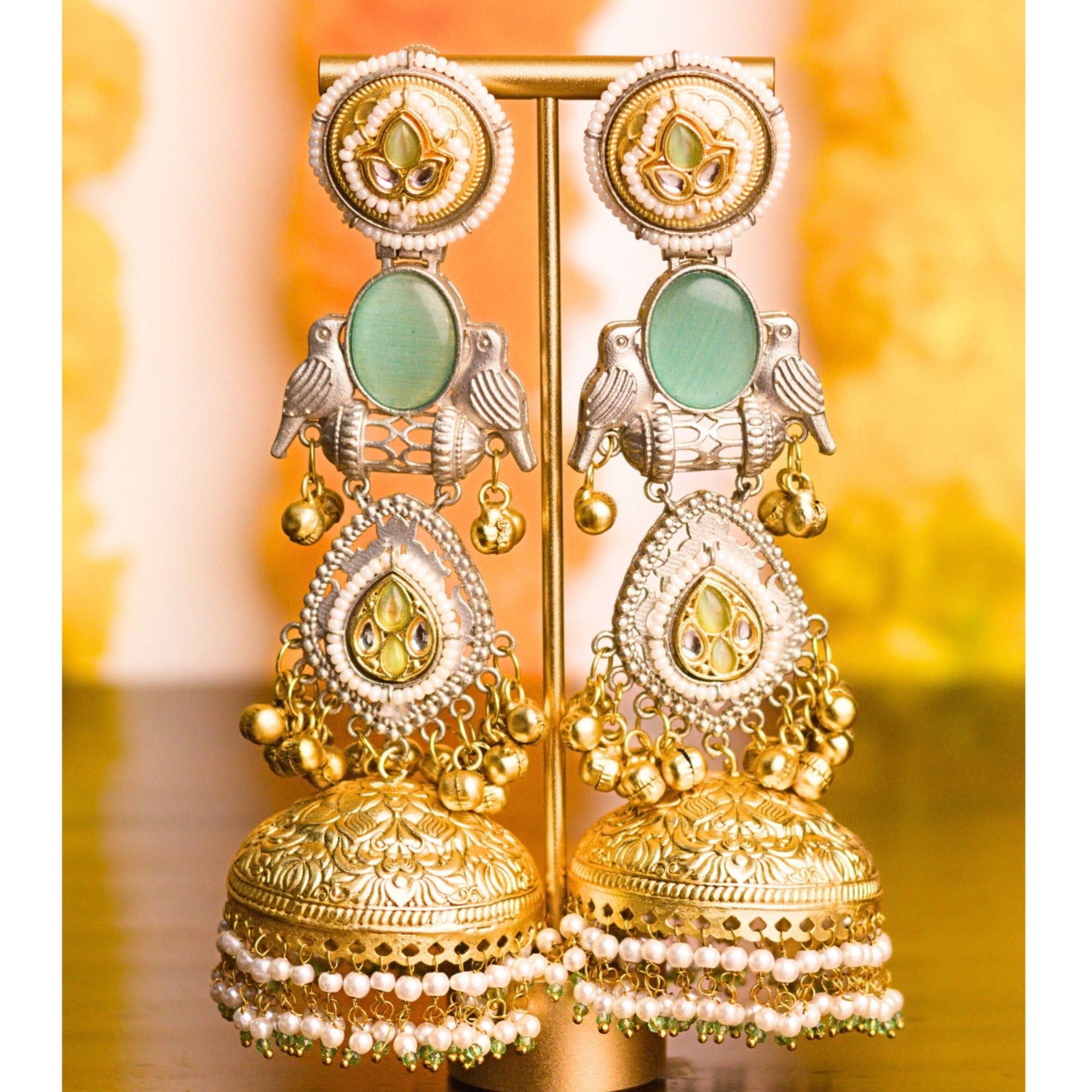 Gold and green earrings on a stand with a blurred background